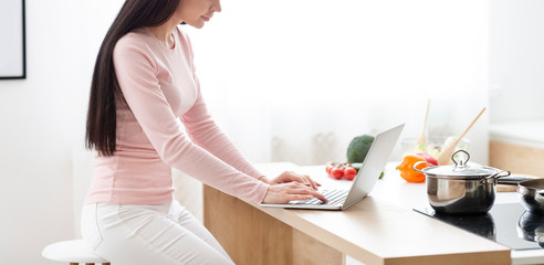 Young woman typing on laptop, sitting at kitchen