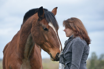 Close up shot of pretty young woman sharing a loving moment with her large cob type bay horse.