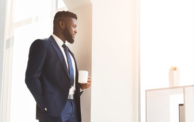 Handsome african businessman drinking coffee near window in office