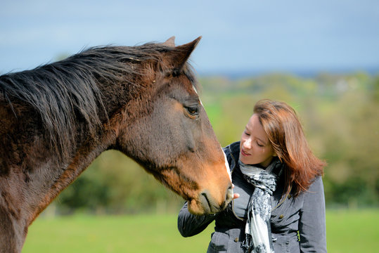 clsoe up shot of pretty young woman and her beautiful bay horse sharing a loving moment in the field.