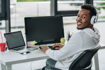 cheerful african american programmer looking at camera while sitting at workplace