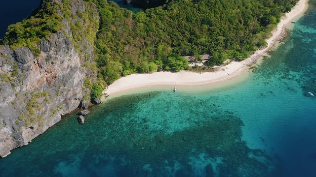 4K Aerial circle fly over tropical beach on Dilumacad or Helicopter island. El Nido, Palawan Philippines. Blue lagoon, intact coral reef, azure clear water and palm trees in morning light