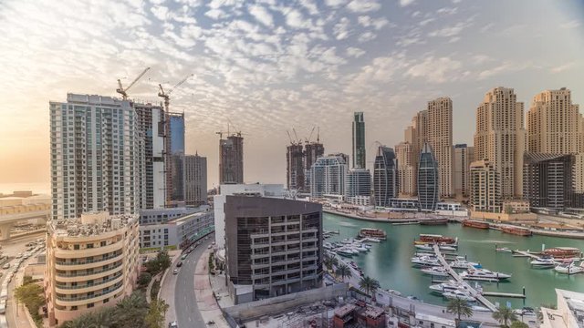 Yachts in Dubai Marina flanked by the Al Rahim Mosque and residential towers and skyscrapers aerial timelapse. Modern high rise skyline with boats and wooden dhows