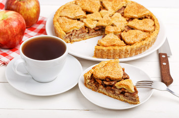 Piece of homemade apple pie with cinnamon and cup of tea on white wooden table. Shallow focus.
