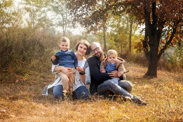 Fototapeta premium Happy family together in autumn garden/park. Parents with their two childrens take the rest in park. Outdoor in full height photo. Happy family concept