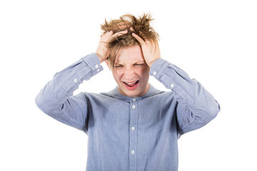 Frustrated teenage boy messing up and pulling his hair, hands to head, looking down shouting and...