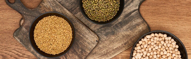 panoramic shot of bowls with beans, grains and chickpea on wooden cutting boards