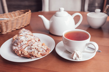 Tea cup, teapot and croissant on table in cafe