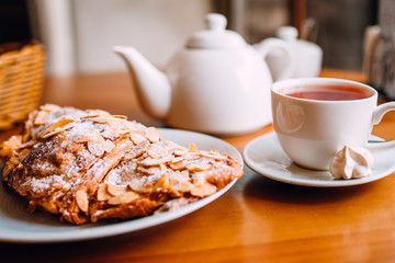 Close up of tea cup, teapot and croissant on table in cafe