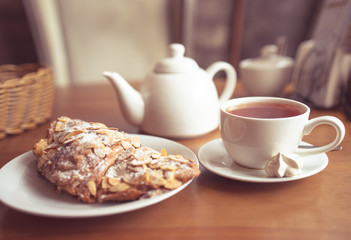 Tea cup, teapot and croissant on table in cafe