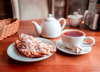 Hot tea, teapot and croissant on table in cafe