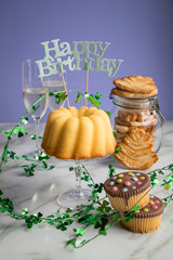 Geburtstagskuchen mit Gugelhupf Kuchen, Muffins, Kekse Gebäck und Sekt mit Happy Birthday Dekoration und Kleeblättern zum Geburtstag
