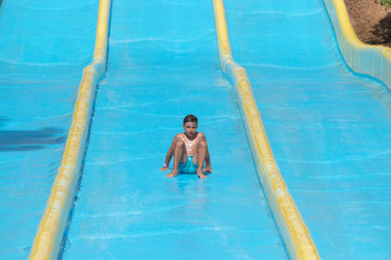 A portrait of  happy boy on water slide in a swimming pool having fun during summer vacation in a...