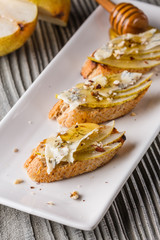 Appetizer bruschetta with pear, honey, walnut and blue cheese on white plate