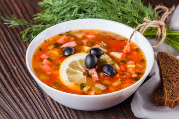 Traditional Russian meat soup Solyanka in bowl on rustic wooden table