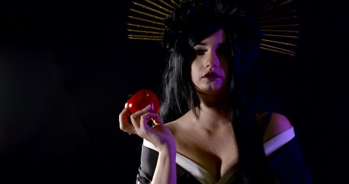 A nightmarish carnival image of a woman in the dark with a crown of shims and a large poisoned red Apple