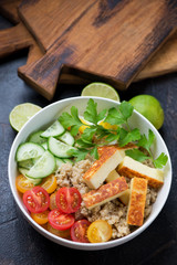 Bowl with quinoa, roasted cheese and fresh vegetables, studio shot on a dark brown stone surface