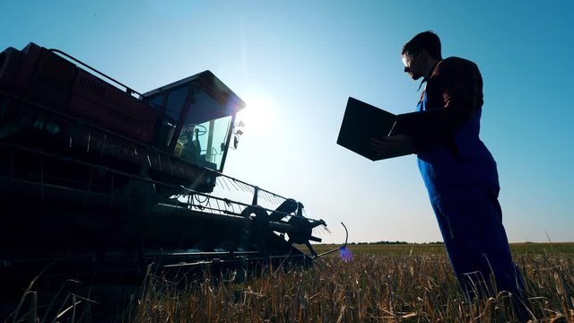 Farmer checks tractor in a field, working with laptop. Farmer on an agricultural field.