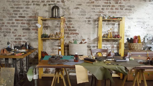 Tracking shot of empty shoemaker studio with leather, supplies, boots and tools on the desk and shelves
