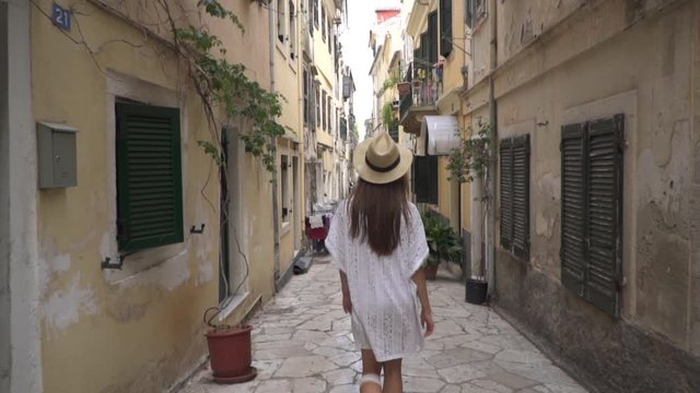 Rear view beautiful girl in white dress walking narrow european streets in old town, Kerkyra, Greek Island Corfu. Summer travel vacation. Adventure.