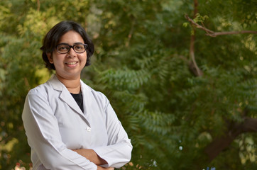 Portrait of a confident young female professional doctor wearing white coat in an outside setting in a park or hospital lawns in New Delhi, India