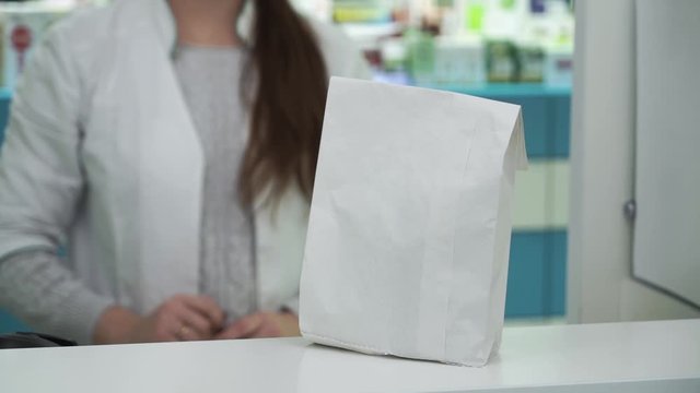 Close-up of a white paper bag with medications given by the female pharmacist to the male customer. Purchase process in the pharmacy. Healthcare and traditional medicine concept.