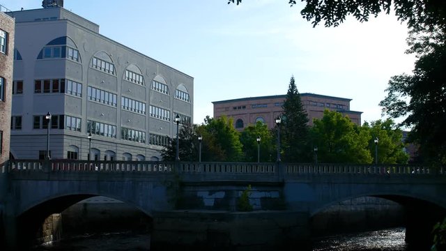 Video of Kenduskeag River water flowing under bridge archways with commercial buildings in the background in the early morning light at Bangor, Maine.