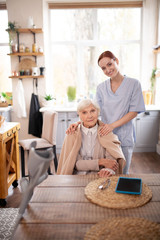 Beautiful pensioner sitting near caregiver