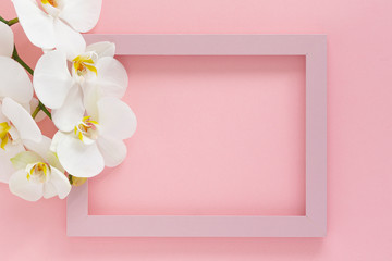 Beautiful White orchid flowers, wooden photo frame on pink background. Pink photo frame and flowers orchids. Empty space for text. Branch of orchid close up. Women's Day, Flower Card. Top view