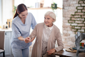 Caregiver smiling while helping aged woman to walk