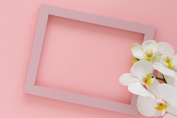 Beautiful White orchid flowers, wooden photo frame on pink background. Pink photo frame and flowers orchids. Empty space for text. Branch of orchid close up. Women's Day, Flower Card. Flat lay.   