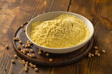 Chickpea flour in white ceramic bowl on wooden table close up