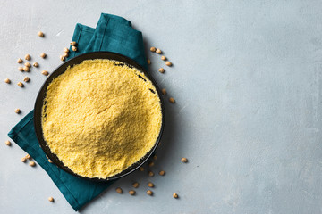 Chickpea flour in black ceramic bowl on light background top view with copy space