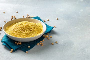 Chickpea flour in white ceramic bowl on light background with spilled chickpeas