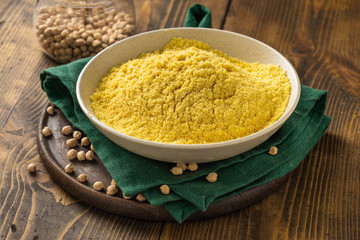 Chickpea flour in white ceramic bowl on wooden table close up