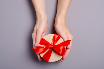 Gift box with red ribbon in hand on gray background, top view