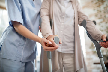 Nurse wearing uniform supporting woman with crutches