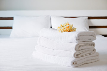 Hotel room with freshly made bed, perfectly clean and ironed snow white sheets, stack of new folded towels in natural sun light. Close up, copy space for text.
