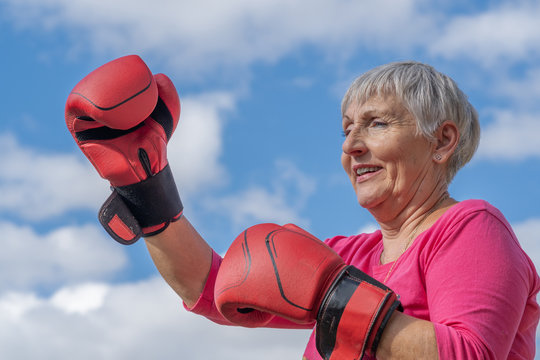 older woman exercising boxing, red gloves and blue sky background