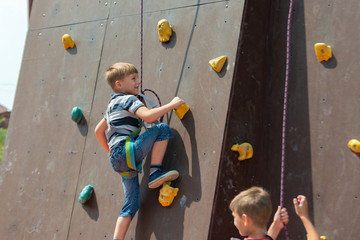 A boy in climbing equipment conquers the top of an artificial tower for climbers in a sports...