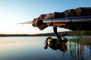Hands of a man in a Urp plan hold a fishing rod, a fisherman catches fish at dawn. Fishing hobby vacation concept. Copy space.