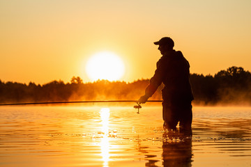 Male fisherman at dawn on the lake catches a fishing rod. Fishing hobby vacation concept. Copy space.