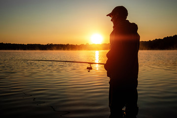 Male fisherman at dawn on the lake catches a fishing rod. Fishing hobby vacation concept. Copy space.