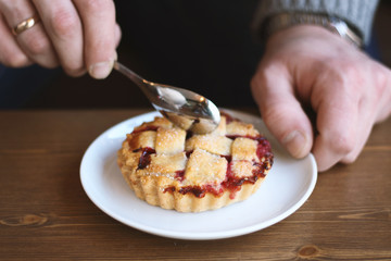 man in grey sweater drinks black lungo americano coffee in winter autumn in coffee shop eating classic american home-made cherry pie on white plate on wooden table. Fall mood instagram style