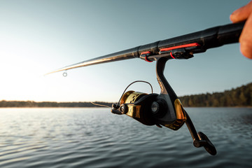 Hands of a man in a Urp plan hold a fishing rod, a fisherman catches fish at dawn. Fishing hobby vacation concept. Copy space.