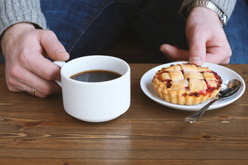 man in grey sweater drinks black lungo americano coffee in winter autumn in coffee shop eating classic american home-made cherry pie on white plate on wooden table. Fall mood instagram style