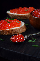 Sandwiches with bran bread, red caviar and butter on black wooden board