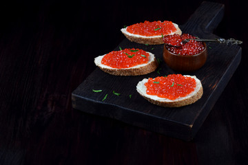 Sandwiches with bran bread, red caviar and butter on black wooden board