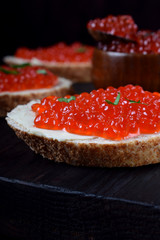 Sandwiches with bran bread, red caviar and butter on black wooden board