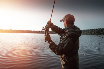 Male fisherman at dawn on the lake catches a fishing rod. Fishing hobby vacation concept. Copy space.